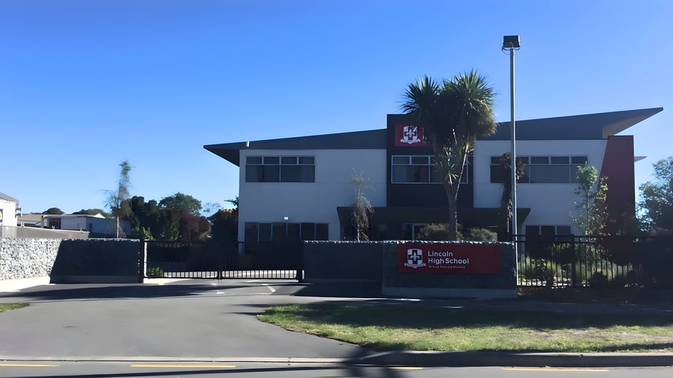 El moderno edificio escolar de la Lincoln High School con el logo y la entrada frente a un cielo despejado.