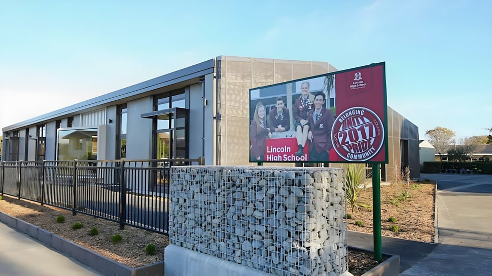 Se puede ver el moderno edificio de vidrio de la Lincoln High School con pared de gabiones y un entorno verde.
