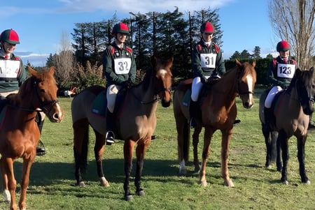Un grupo de jinetes en uniforme sobre caballos está en un campo de hierba en el terreno de la Lincoln High School.