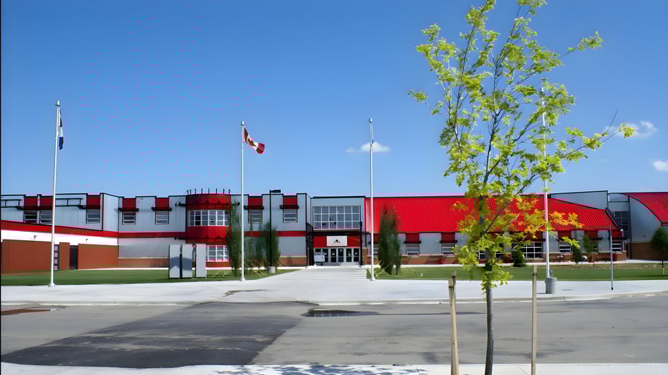 El moderno edificio de la Lindsay Thurber Comprehensive High School con banderas ondeando y árboles en primer plano.