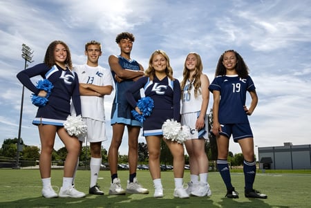 Un grupo de animadoras de la Linfield Christian School se encuentra juntas en un campo cubierto de hierba bajo un cielo nublado.