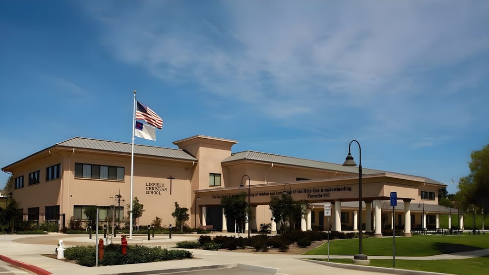 El edificio de dos pisos de la Linfield Christian School con la bandera americana y la bandera surcoreana bajo el cielo despejado.