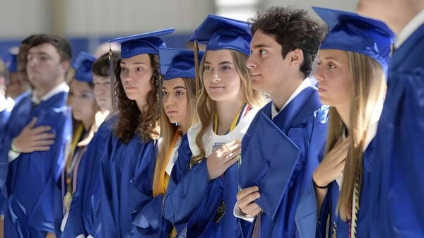 Graduadas y graduados del Lisgar Collegiate Institute en togas de graduación azules posan juntos frente a un fondo azul y blanco.