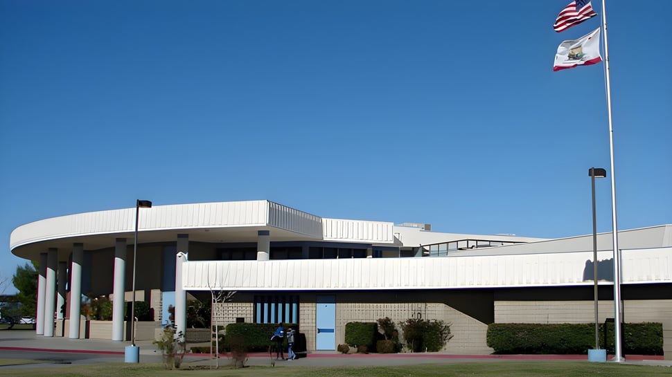 El moderno edificio blanco de la Littlerock High School con un techo curvo y una bandera americana delante.