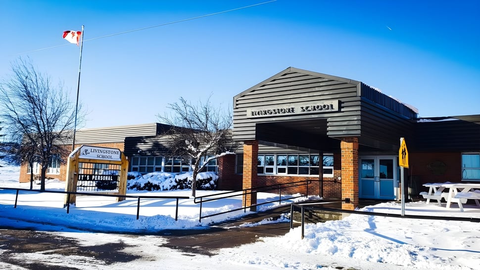 El edificio escolar de madera de la Livingstone School se encuentra en un paisaje nevado con árboles desnudos y cielo azul.