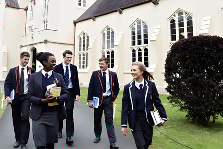 Un grupo de estudiantes en uniforme escolar camina juntos por el patio del Llandovery College con arquitectura gótica.