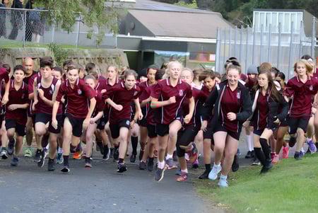 Estudiantes de Logan Park High School caminan juntos con ropa uniforme por un camino junto a áreas verdes y edificios.