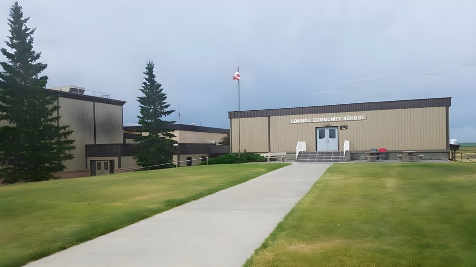 El moderno edificio de la Lomond Community School con la bandera canadiense está rodeado de césped y altos pinos.