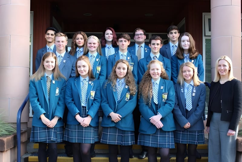 Un grupo de alumnas está de pie en uniforme escolar frente a un edificio con columnas en el campus de la Lomond School.