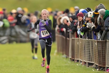 Una corredora corre en un campo de hierba frente al público en el terreno de la Longfields-Davidson Heights Secondary School.