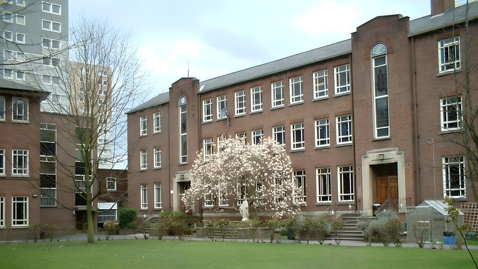 Edificio de ladrillo de varios pisos con un árbol en flor y una superficie de césped en el campus del Loreto College Cavan.