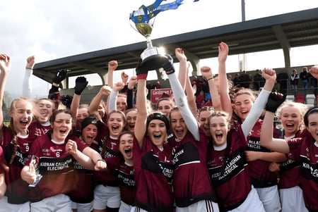 Estudiantes del Loreto College Cavan celebran su victoria con un trofeo en una arena deportiva.