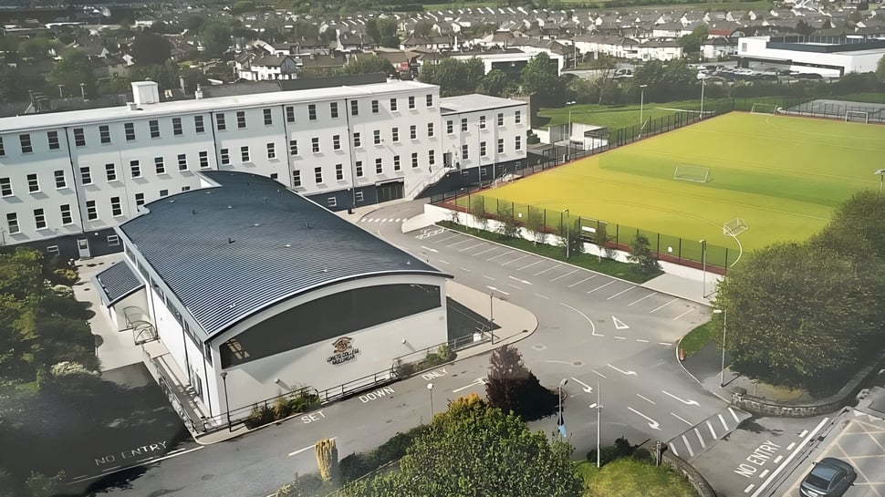 El gran edificio de varios pisos con techo abovedado en el terreno del Loreto College Mullingar está rodeado de edificios más pequeños y un prado.