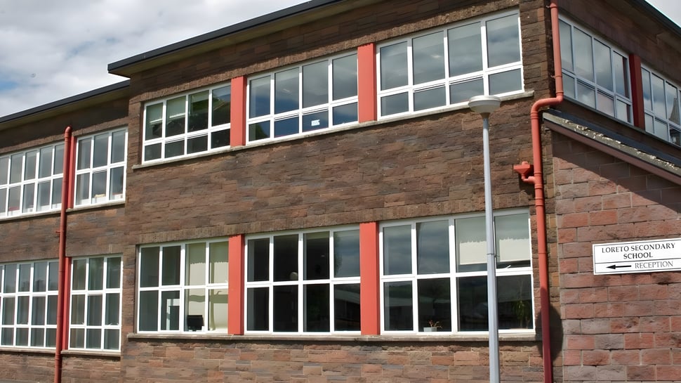 El edificio de ladrillo de varios pisos de la Loreto Secondary School en Cork con grandes ventanas y acentos rojos frente a un cielo nublado.