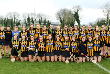 Un gran grupo de jóvenes deportistas está de pie sobre el césped de la Loreto Secondary School frente a árboles y edificios.