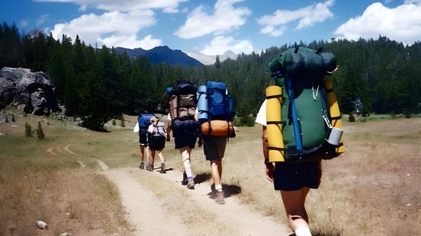 Un grupo de estudiantes de la Loreto Secondary School camina con grandes mochilas por un sendero en el bosque en las montañas.