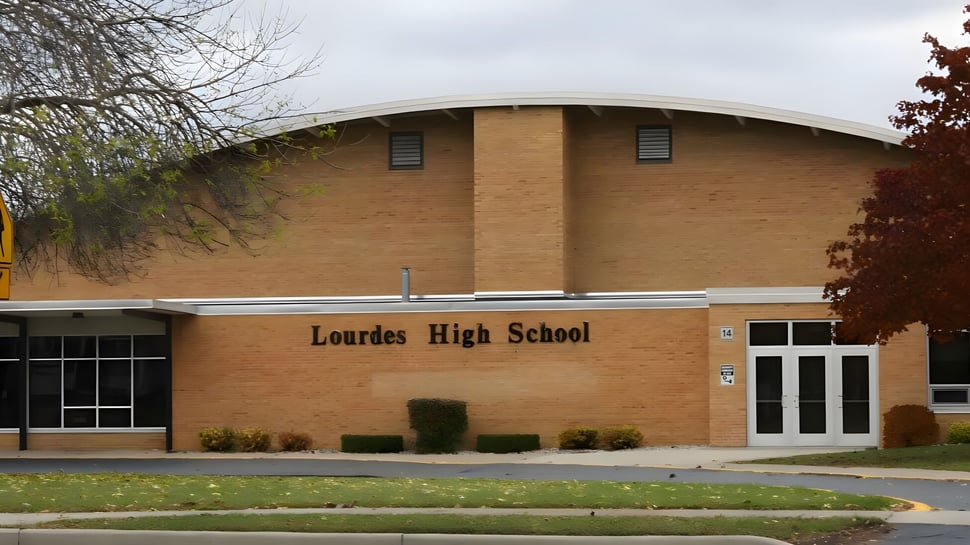 El edificio de ladrillo de Lourdes Academy está rodeado de árboles y una zona verde.