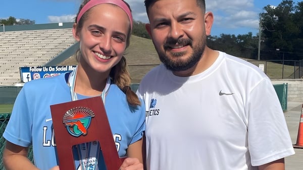 Una estudiante y un profesor de Lourdes Academy están juntos frente a un campo deportivo en el recinto escolar.