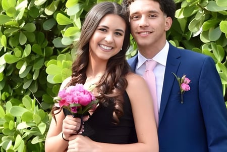 Una pareja sonríe frente a un fondo verde con flores en el campus de Lourdes Academy.