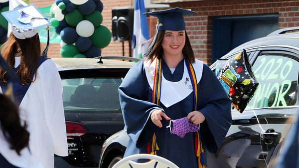 Una alumna de la Lowell Catholic High School lleva una toga de graduación y sostiene un diploma en la mano.