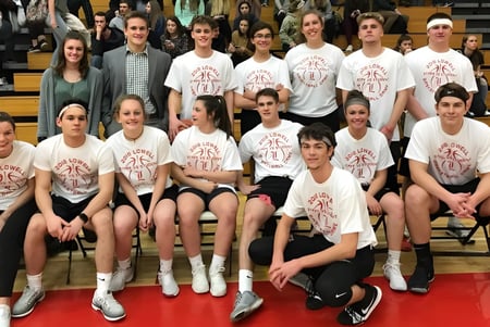 Un grupo de estudiantes de la Lowell High School está sentado en un gimnasio y lleva camisetas deportivas blancas uniformes.