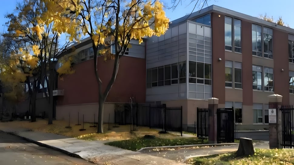 El moderno edificio del Lower Canada College está rodeado de árboles con hojas amarillas de otoño y muestra un camino pavimentado en primer plano.
