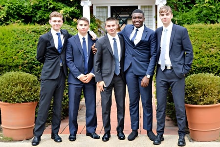 Un grupo de estudiantes de la Luckley House School está vestido formalmente en un jardín bien cuidado con plantas en macetas y setos.