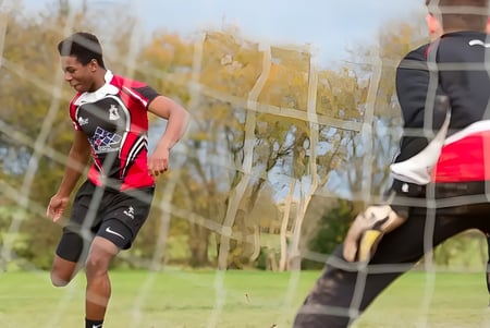 Un hombre con una camiseta roja y negra corre sobre un campo verde en el terreno de la Lucton School.