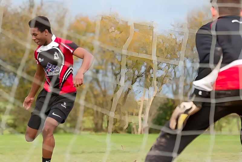 Un hombre con una camiseta roja y negra corre sobre un campo verde en el terreno de la Lucton School.