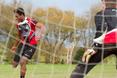 Un estudiante masculino de la Lucton School corre en un campo de hierba con árboles y edificios de fondo.