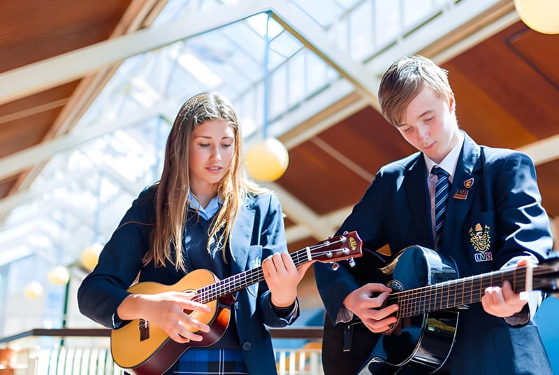 Dos alumnas de LVS Ascot tocan la guitarra en una habitación luminosa con grandes ventanas.