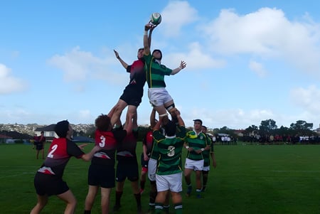 Un grupo de estudiantes juega rugby en el campo deportivo del Lynfield College bajo un cielo azul con nubes.