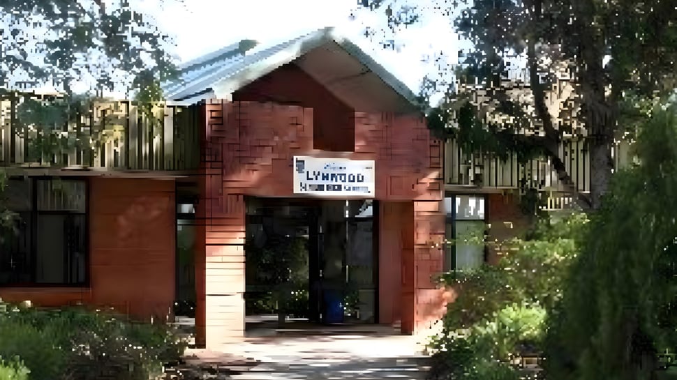 El edificio de ladrillo de la Lynwood Senior High School está en el bosque con un camino pavimentado hacia la entrada.
