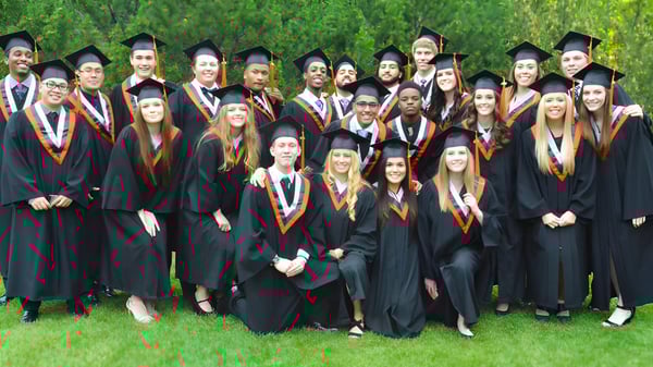 Un grupo de graduados de la M.E. LaZerte Composite High School está de pie en un césped frente a un paisaje verde con vestimenta académica.