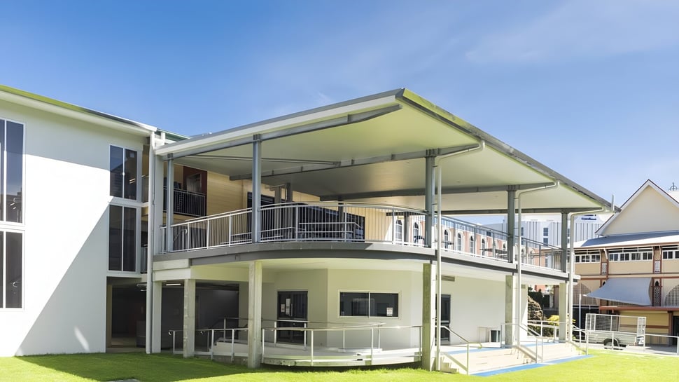 Un moderno edificio residencial con balcón y área de césped frente al cielo despejado en el terreno de la Mabel Park State High School.