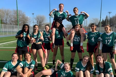 Un grupo de jóvenes deportistas en camisetas verdes y negras posan en un campo de la Macdonald High School.