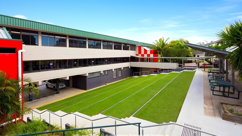 El moderno edificio escolar de la MacGregor State High School con áreas verdes y palmeras en primer plano.