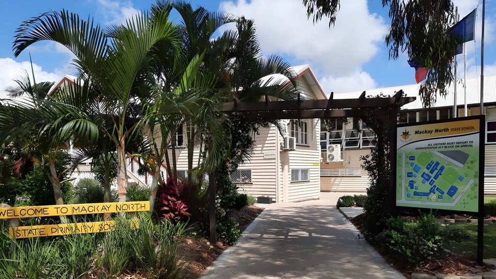 El edificio de la Mackay North State High School está rodeado de vegetación tropical con palmeras.