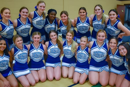 Un grupo de jóvenes animadoras en uniformes azules y blancos posan juntas en una sala del campus de la Mackay North State High School.