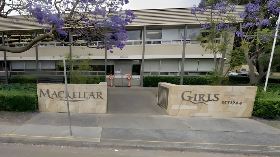 El edificio con el letrero Mackellar Girls Campus está rodeado de árboles con flores violetas.
