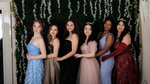 Cinco jóvenes mujeres de la Maharishi School posan juntas frente a un fondo de flores con diferentes vestidos formales.