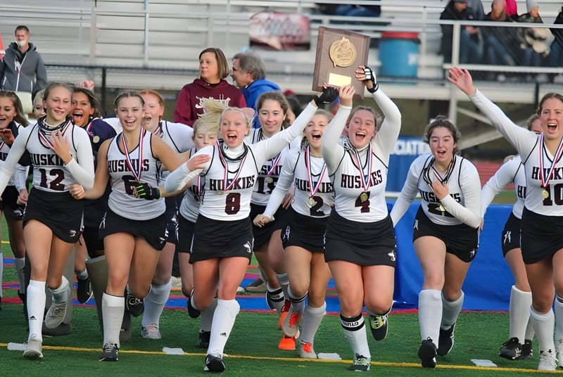 Un grupo de jóvenes atletas del Maine Central Institute celebra en el campo deportivo la victoria de un trofeo.
