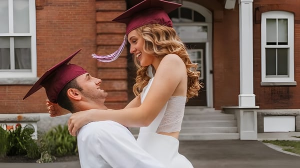 Una joven pareja en toga de graduación se abraza frente a un edificio de ladrillo en el campus del Maine Central Institute.