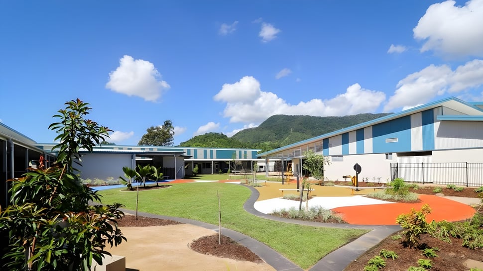 El moderno y colorido edificio escolar de la Malanda State High School con un cuidado exterior y un paisaje montañoso de fondo.