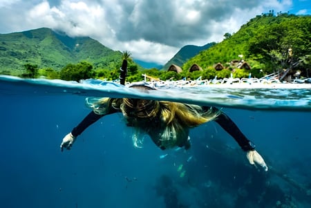 Una estudiante de la Maleny State High School nada en el agua azul clara frente a montañas verdes y un cielo nublado.