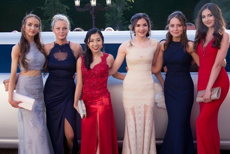 Seis mujeres elegantemente vestidas del Malvern College posan frente a una limousine en el campo.