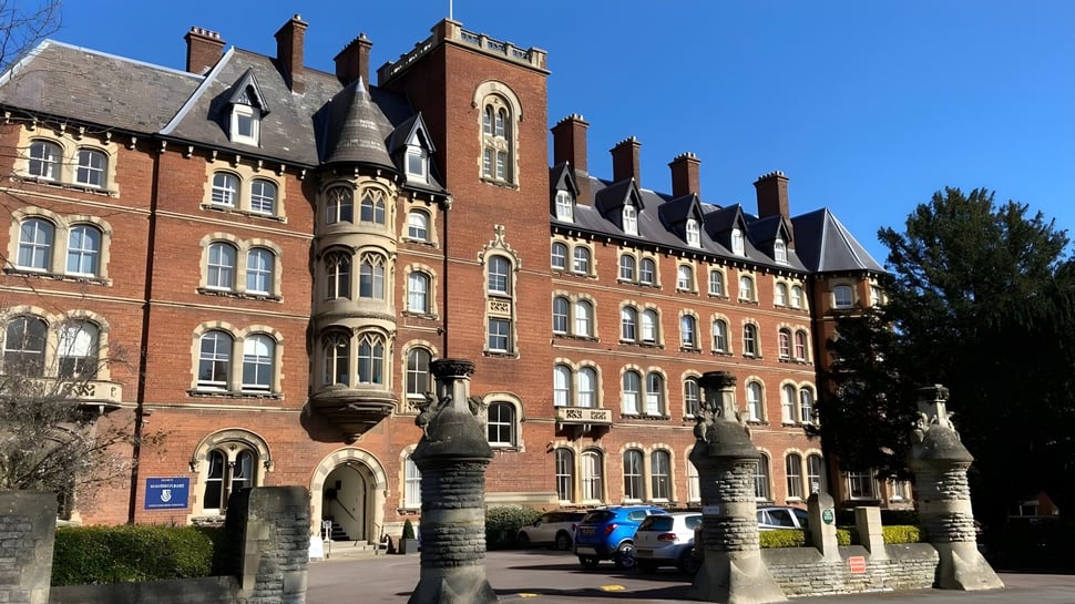 El histórico edificio principal de la Malvern St. James Girls' School con una torre y rodeado de árboles bajo un cielo despejado.