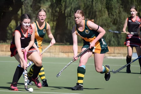Un grupo de alumnas del Manea Senior College juega un partido de hockey sobre césped en el campo deportivo verde.