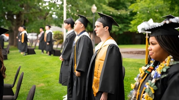 Un grupo de graduados de la Mannahouse Christian Academy está de pie en ropa académica en el campus sobre un césped.