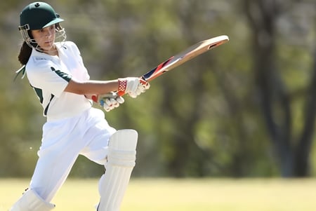 Un estudiante de la Manor House School golpea la pelota durante el cricket en el campo deportivo con árboles al fondo.